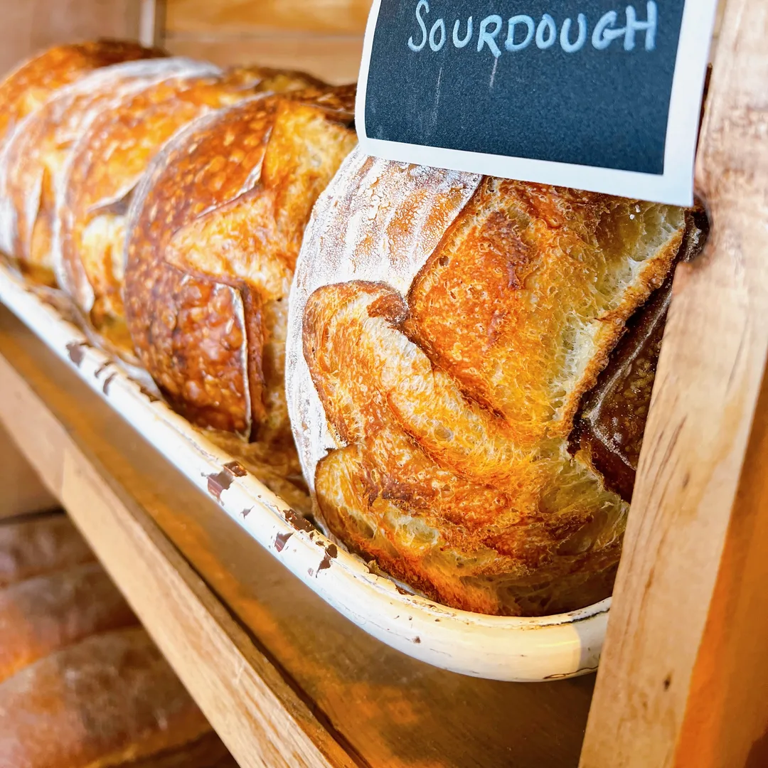 Scored sourdough loaves on the bread shelf under a chalkboard sign