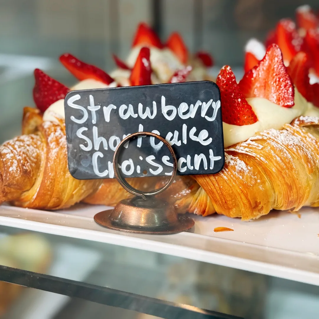 Strawberry shortcake croissants in the case behind a hand-lettered chalkboard sign